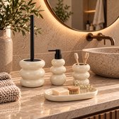 Beige badkamerset van keramiek: toiletborstel, zeepdispenser, tandenborstelhouder en zeepbakje met ronde vormen.