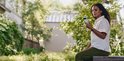 Vrouw zit buiten in een tuin en gebruikt haar smartphone met een Fitbit Edge aan haar pols.