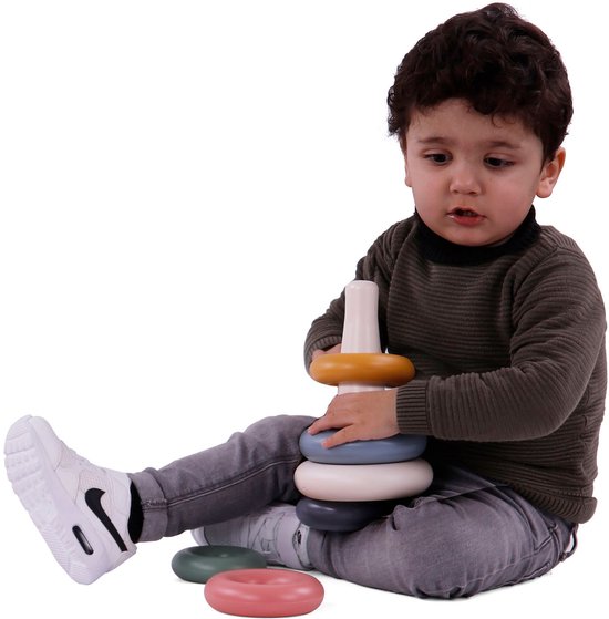 Peuter met donkerbruin haar speelt met een set pastelkleurige stapelringen op een witte achtergrond.