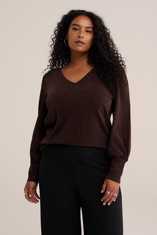 Model draagt een bruine glittertop met V-hals en pofmouwen op een zwarte broek.