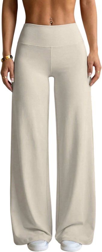 Model in beige flared broek en bijpassende top tegen een zwarte achtergrond.