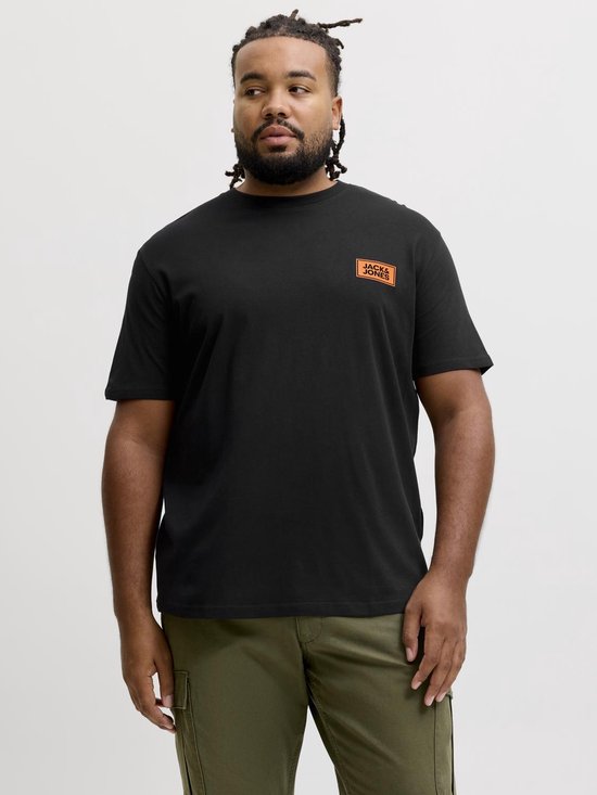 Een man met vlechtjes draagt een zwart T-shirt met oranje logo op de borst en een olijfgroene cargobroek.