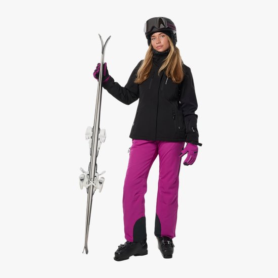 Vrouw met zwarte ski-jas, paarse skibroek, helm, skibril en ski's.