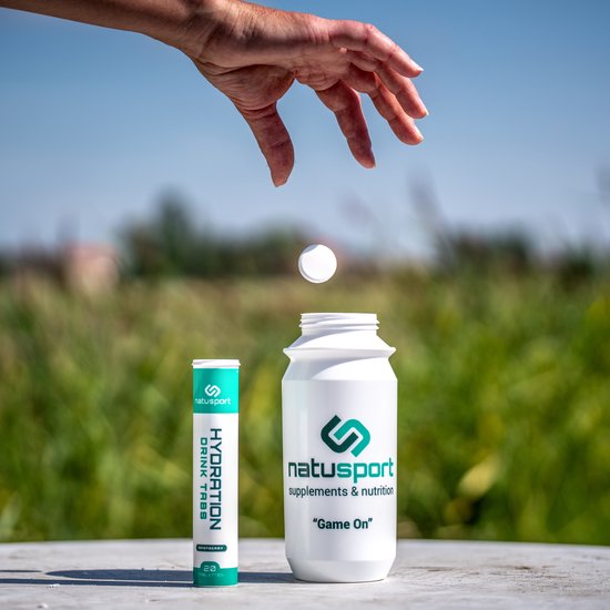Hand die een bruistablet boven een open Natusport fles laat vallen, met een tube Hydration Tabs ernaast.
