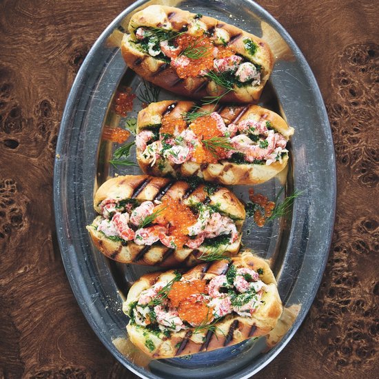 Quatre petits pains grillés garnis de salade de homard, œufs de saumon et aneth sur un plat ovale.
