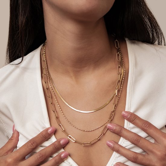 Model met handen op de borst, toont een gelaagde goudkleurige ketting met diverse schakels.