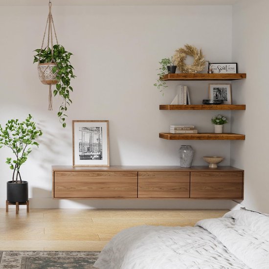 Een slaapkamer met een tv-meubel met zwevende planken erboven en een hangplant.