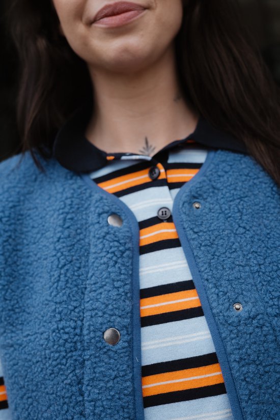 Close-up van een donkerblauwe teddy bodywarmer met drukknoopsluiting, gedragen over een gestreept shirt.