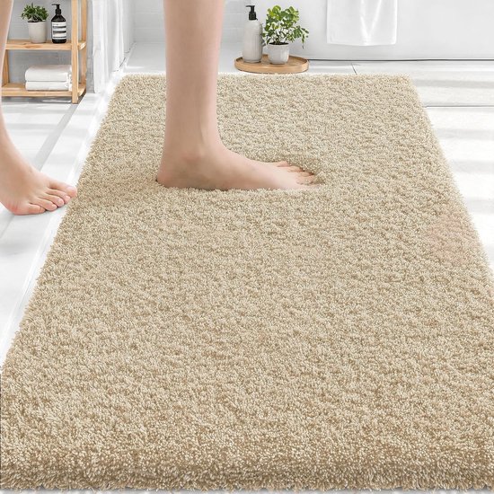 Zachte, beige badmat van 60 x 100 cm met een antislip onderkant, waarop een voet staat.