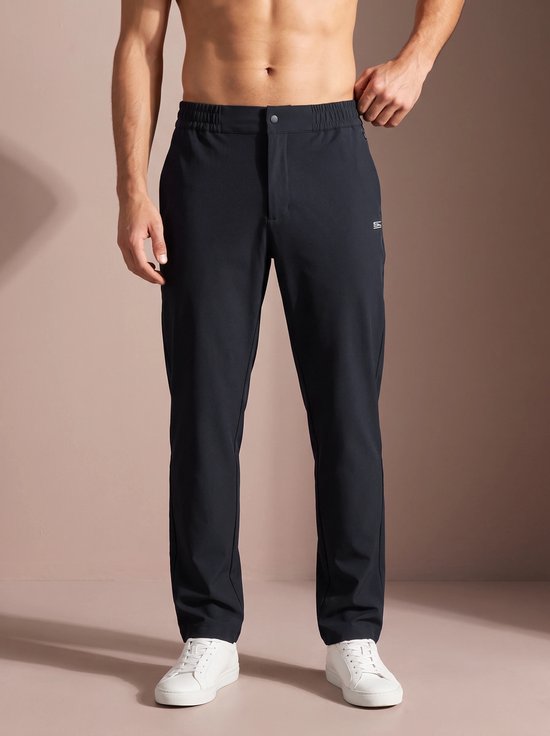 Man draagt een donkerblauwe sportbroek met het 'SJS' logo en witte sneakers.