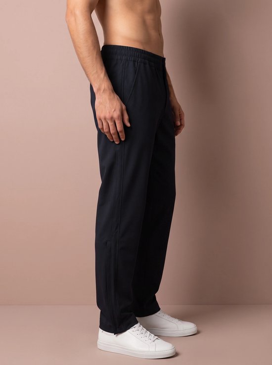 Zijzicht van een man die een donkerblauwe sportbroek draagt, met witte sneakers.