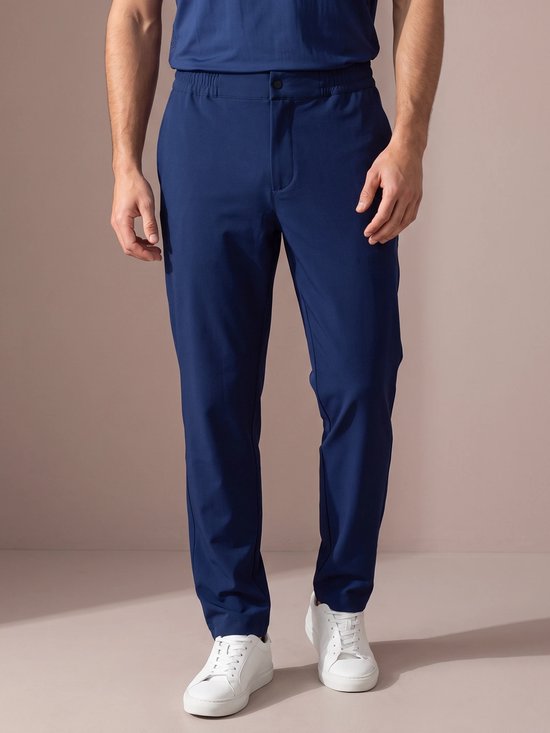 Marineblauwe sportbroek met elastische tailleband, knoopsluiting en witte sneakers.