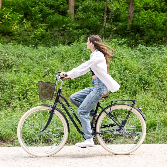 Vrouw die op een zwarte RCB-fiets met mand rijdt op een bospad langs groen struikgewas.