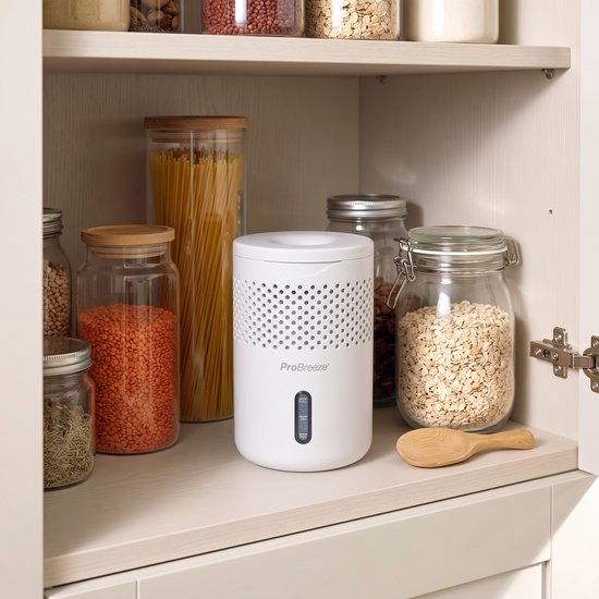 Witte Pro Breeze vocht collector in een kast tussen potten met eten, met een perforatie patroon aan de bovenzijde.