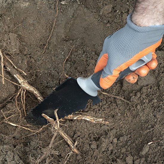 Hand met oranje-grijze handschoen gebruikt zwarte spade met gekartelde rand om door wortels in de aarde te snijden.