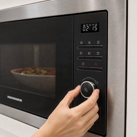 Close-up van een Heinner inbouwmagnetron. Een hand draait aan de knop van het zwarte bedieningspaneel met LED-display.