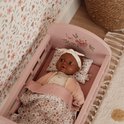 Baby-doll in een roze poppenbed met bloemenprint dekentje en hoofdband.