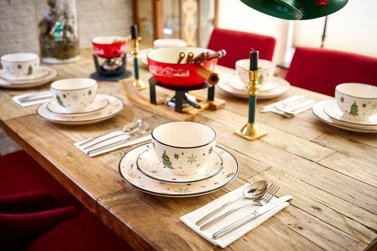 Gedekte tafel met kerstservies: borden en kommen met kerstboom- en sneeuwvlokmotief, rode fonduepan.