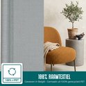 Grijze raamfolie met textielstructuur, naast een gele fauteuil en een plant. "100% Raamtextiel".
