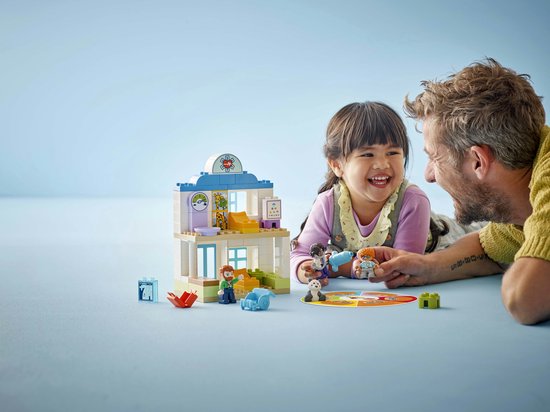Vader en dochter lachen en spelen met LEGO Duplo dokterscentrum. Op de grond liggen diverse onderdelen.