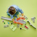 Jongetje legt LEGO Duplo treinbaan aan met losse oranje bruggen, grijze rails en groene onderdelen.