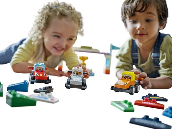 Deux enfants jouent avec des voitures de course et des pièces LEGO Duplo sur le sol.
