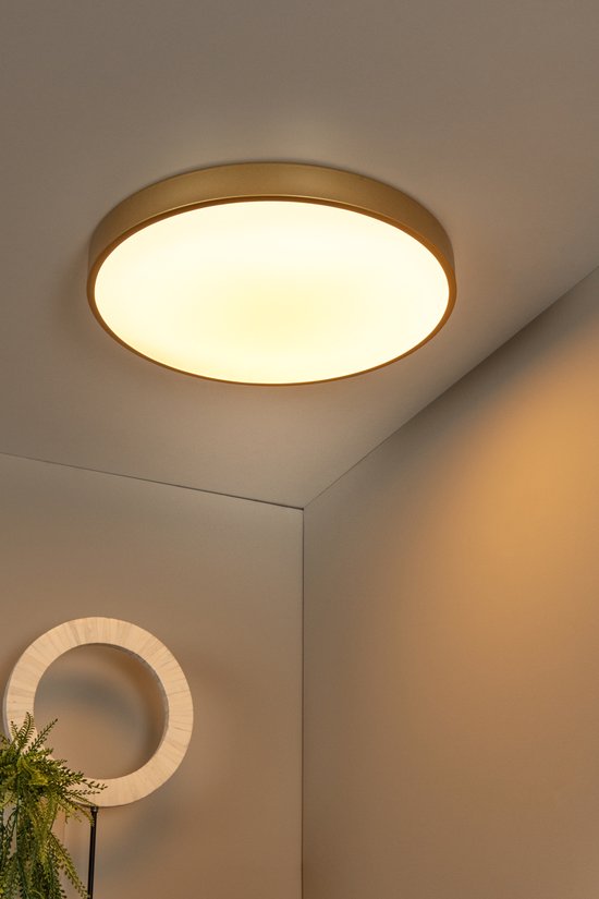 Ronde, mat gouden plafondlamp verlicht een hoek van een kamer.