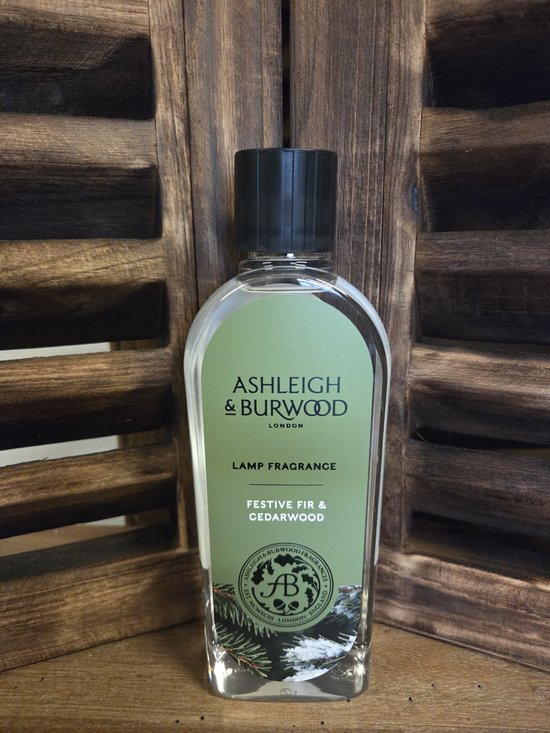Fles Ashleigh & Burwood lampolie Festive Fir & Cedarwood met groen etiket op een houten achtergrond.