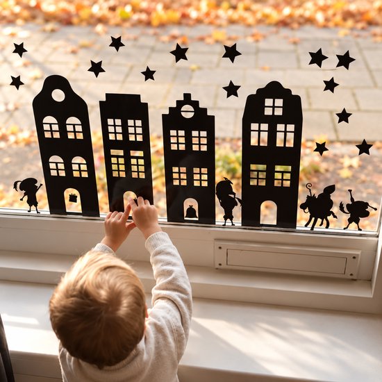 Zwarte statische raamstickers met Sinterklaasfiguurtjes en huizen tegen een raam met herfstbladeren.