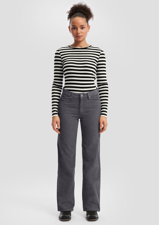 Model draagt een grijze corduroy broek met wijde pijpen en een zwart-wit gestreept shirt.