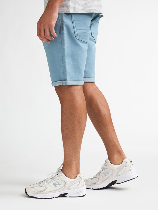 Lichtblauwe denim shorts met opgerolde zoom, gedragen door een man met witte sneakers.