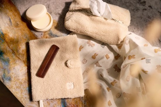 Collectie verzorgingsproducten: pluche beige etui, kam, potje crème en hydrofiele doek met dierenprint.