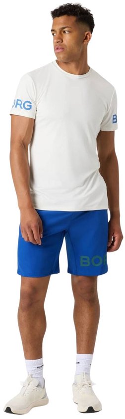 Man in wit sportshirt met blauwe tekst op de mouwen, en een blauwe short.
