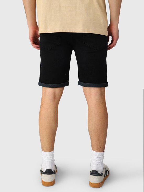Achterkant van zwarte denim shorts met opgerolde zomen, gedragen met een beige T-shirt en witte sneakers.
