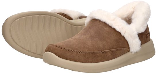 Een paar bruine Skechers instapsloffen met witte bontvoering, inclusief het profiel van de beige zool.