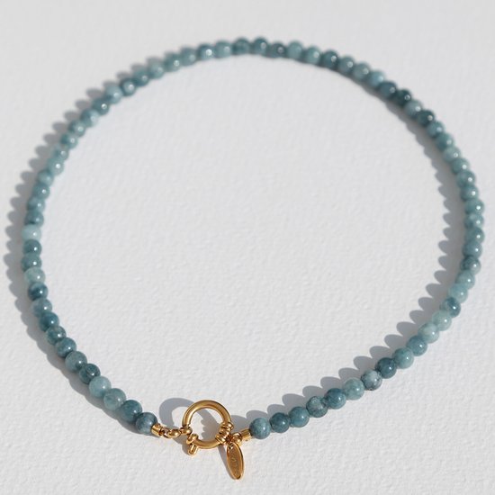 Collier de perles en pierre bleue avec un fermoir doré et un petit pendentif rond sur fond blanc.