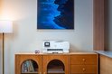 Witte HP Envy All-in-One printer met kleurenscherm op een houten dressoir, naast twee inktcartridges.