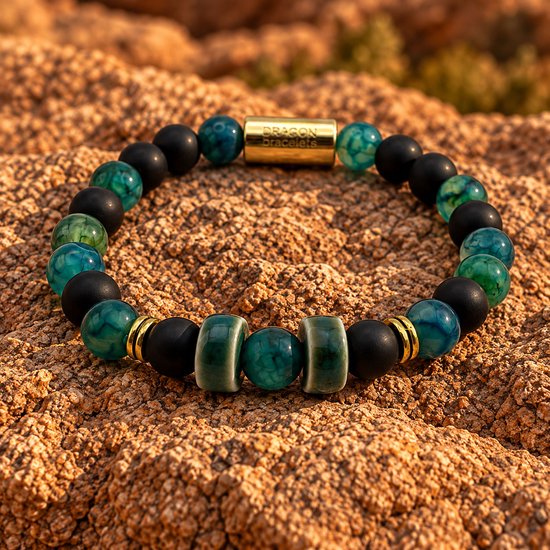 Armband met zwarte matte kralen, groene agaat, geglazuurde keramische ringen en gouden details op een rotsachtige ondergrond.