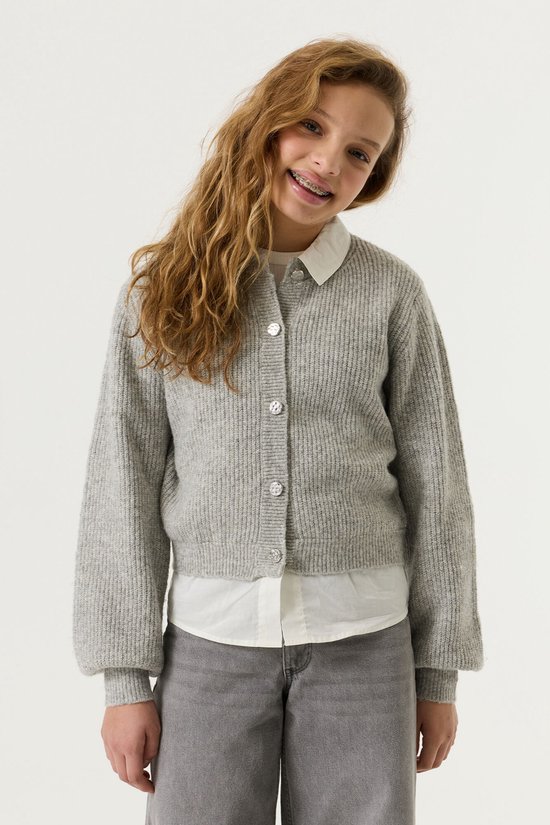 Le modèle porte un gilet gris à boutons avec un col blanc, associé à un jean gris.