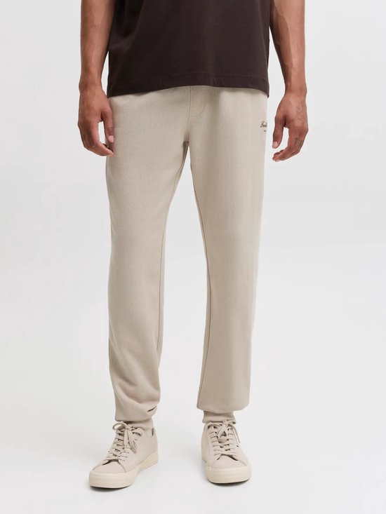 Close-up van beige sweatpants met kleine 'Jack & Jones' tekst op de heup, gedragen met beige sneakers.