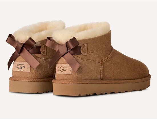 Achterkant van twee cognackleurige UGG-laarzen met strikdetails en het UGG-logo op een suède patch.