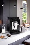 Zwarte Krups espressomachine op een keukenblad met melkfles en koekjes.