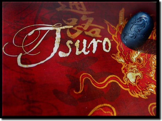 Close-up van een blauwe Tsuro-steen met drakenafbeelding naast de 'Tsuro' tekst op een rode achtergrond.
