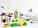 Een kinderkamer met LEGO-opbergdozen in groen, geel, lichtblauw en wit. Een bed met gestreept beddengoed en LEGO-hoofden opgestapeld op een kast.
