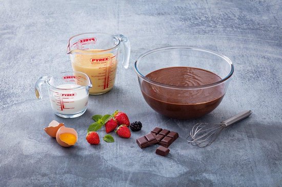 Glazen mengkom met chocolademengsel, twee glazen maatbekers met melk en room, eieren, aardbeien, braam en chocolade.