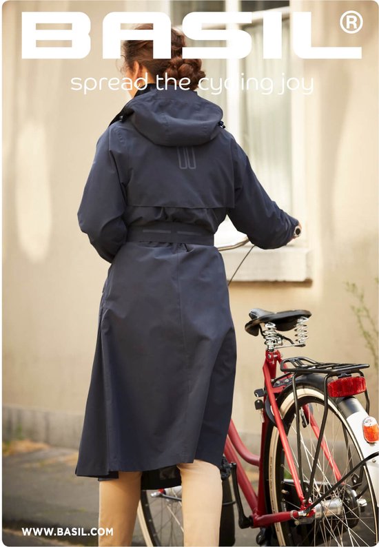 Vrouw met lange donkerblauwe jas met capuchon en ceintuur, staand naast een fiets.