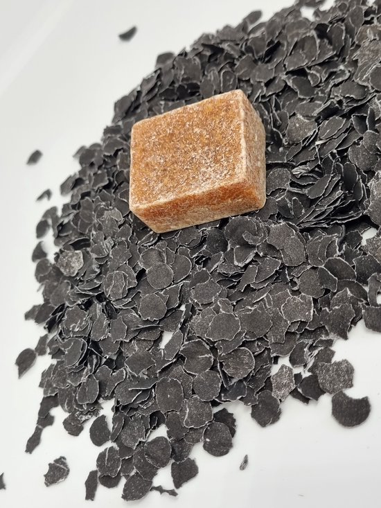 Een bruin, korrelig amberblokje op een witte achtergrond met zwarte schilfers.