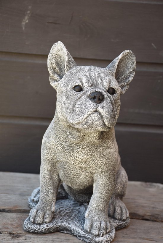 Statue grise en béton d'un bouledogue français aux grandes oreilles et aux yeux perles, regardant la caméra.