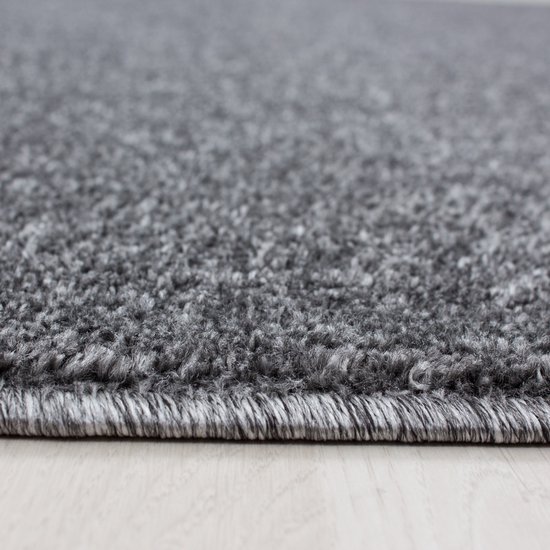 Gros plan détaillé d'un tapis gris foncé à poils courts, avec une texture de fibres fines.