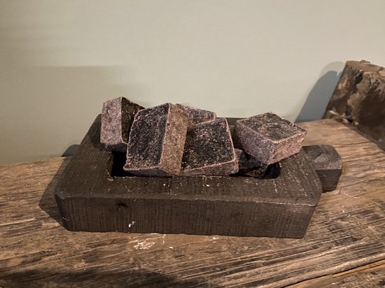 Meerdere donkergrijze, vierkante amberblokjes met een ruw oppervlak, gelegen in een zwart houten bakje.